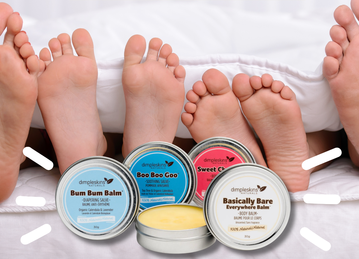 Dimpleskins Naturals balm products displayed with bare feet on white bedding. The image features three round metal balm tins in the foreground with blue, teal, and pink labels, alongside a large promotional text banner at the top.