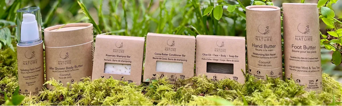 A set of natural skincare products from the brand NATURE, including a hand cream, foot cream, and hand butter in kraft paper packaging, arranged on green moss in an outdoor forest setting.