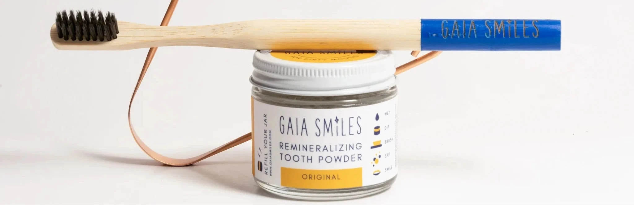 Gaia Smiles tooth powder jar with a wooden toothbrush and copper-colored wire loop on a clean white background.
